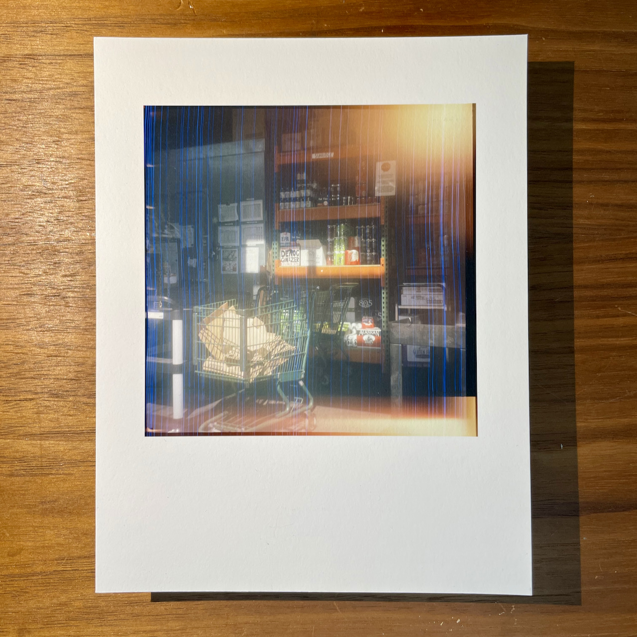 A photo print of the back stock room of a grocery store with sunlight filtering in. There’s light leak in the corner and the film emulsion was horribly scratched